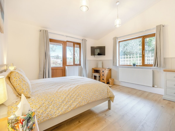 Un dormitorio con cama, escritorio, televisor y ventana con cortinas.