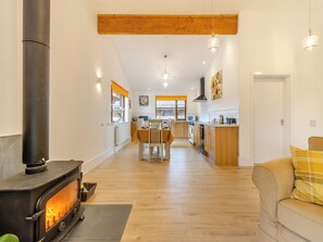A spacious living area with a wood-burning stove, a dining table with chairs, a kitchen with wooden cabinets, and a sofa with a plaid cushion. - Lime Lodge - UK42547 (Llandrindod Wells)