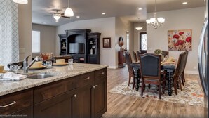 Una cocina amplia con gabinetes de madera oscura, encimera de granito y comedor con alfombra floral y sillas de madera.