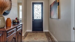 Un pasillo con una puerta oscura, un tapete estampado y un jarrón decorativo sobre un aparador.