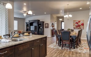A spacious kitchen with dark wood cabinets, a granite countertop, and a dining area with a floral rug and wooden chairs.