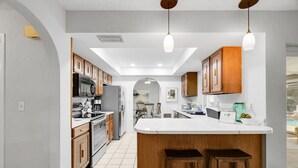 A modern kitchen with wooden cabinets, a central island with stools, and pendant lighting.
