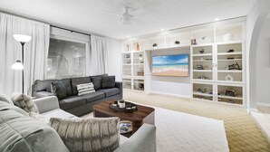 A modern living room with a grey sofa, a coffee table, and a bookshelf filled with decorative items.