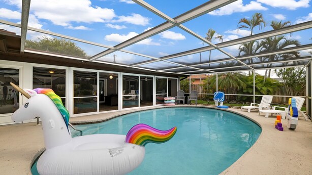 An indoor pool with a unicorn float, glass doors, and outdoor seating.