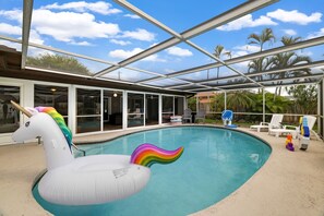 Une piscine intérieure avec un flotteur en forme de licorne, des portes vitrées et un espace extérieur aménagé pour s’asseoir.