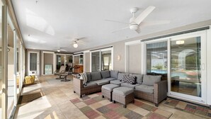 A spacious living area with a large sectional sofa, a ceiling fan, and a view of a swimming pool through glass doors.