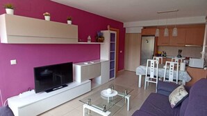 Een moderne woonkamer met een flatscreen televisie, een glazen salontafel en een paarse bank.