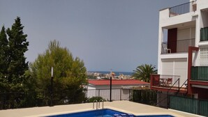 Een rechthoekig zwembad met een blauwe binnenkant, omgeven door een beigekleurig terras. Er zijn twee metalen ladders om het zwembad te bereiken. Het zwembad bevindt zich op een dak terras met uitzicht op de stad en de zee.