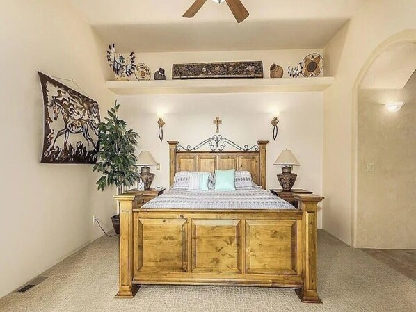 Une chambre à coucher avec un lit en bois, des lampes de chevet, une croix sur la tête de lit et une étagère murale décorative.