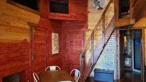 Interior de cabana de madeira com área de refeições, escada e decoração com moinho de vento.