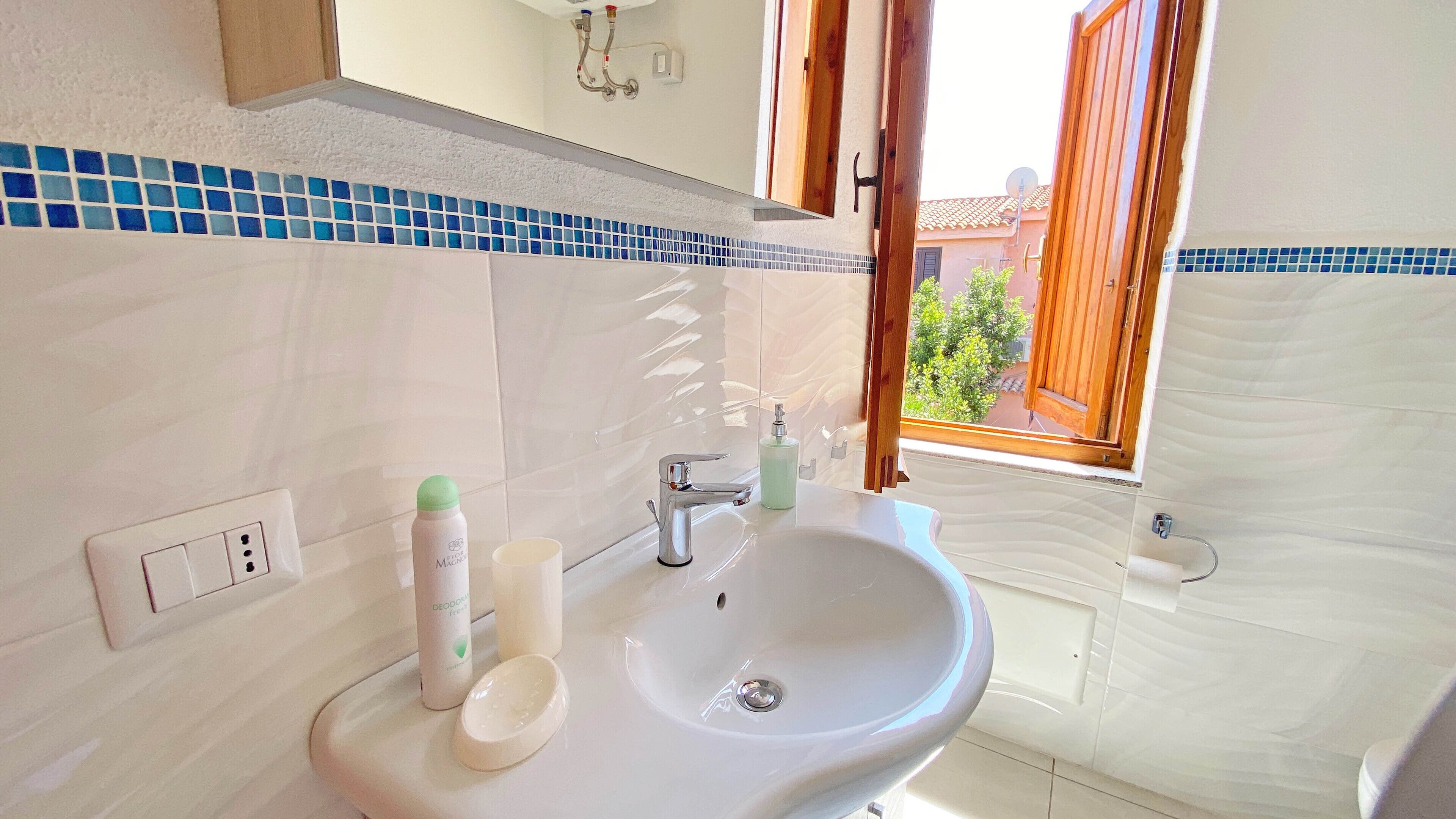 A bathroom with a white sink, a mirror, and a window with a view of buildings and greenery outside.