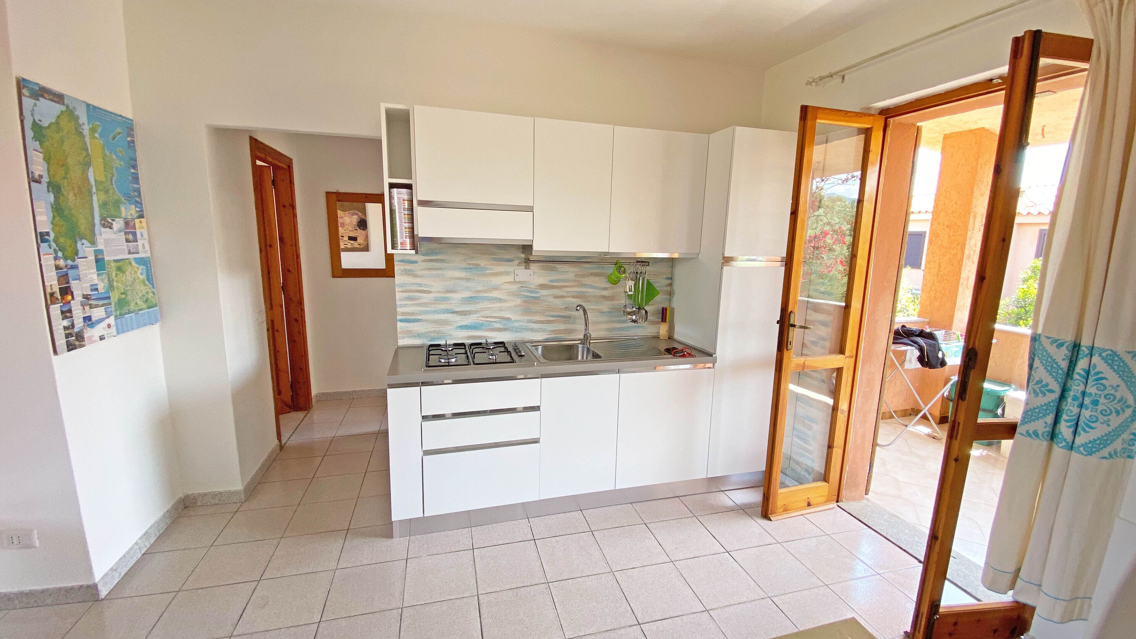 Una cocina compacta con armarios blancos, estufa a gas y un lavamanos.
