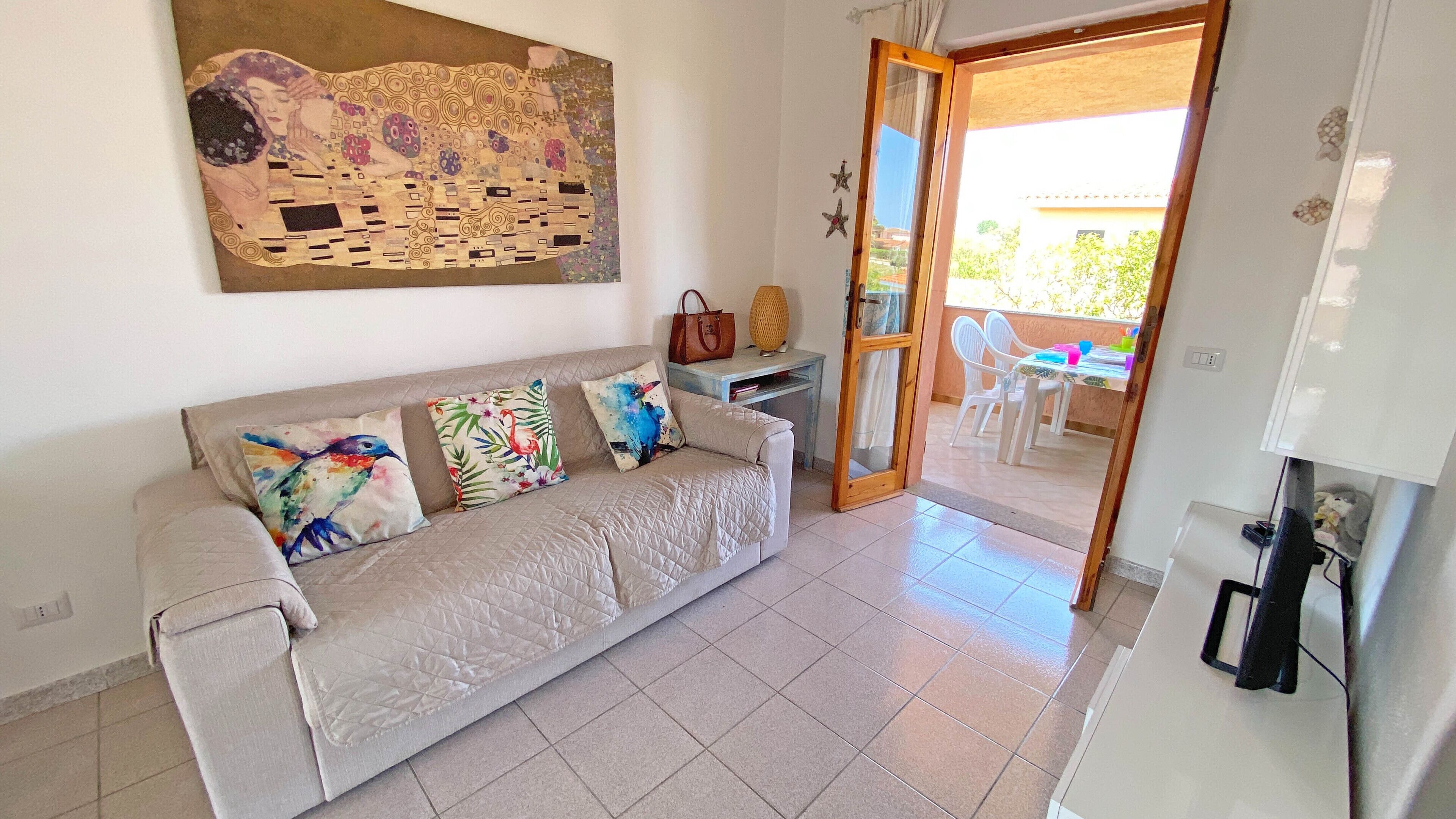 Un salón con un sofá color beige, almohadones de colores, un cuadro en la pared y vistas al balcón exterior.