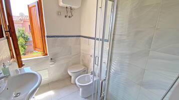 A bathroom with a sink, toilet, bidet, and a glass shower enclosure.