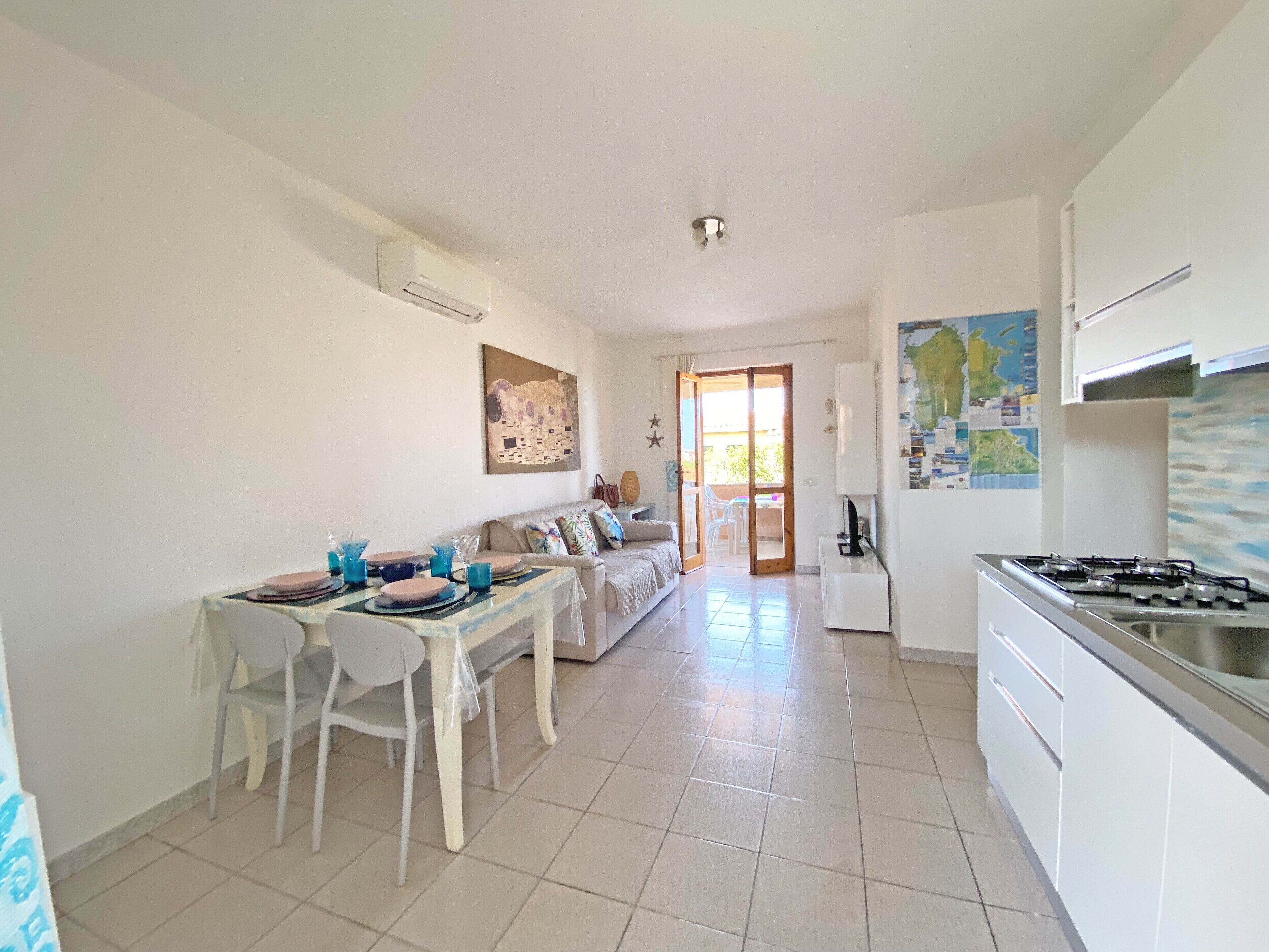 Een moderne keuken met een gasfornuis, een eethoek met een tafel en stoelen, een bank en een schuifpui naar een balkon.