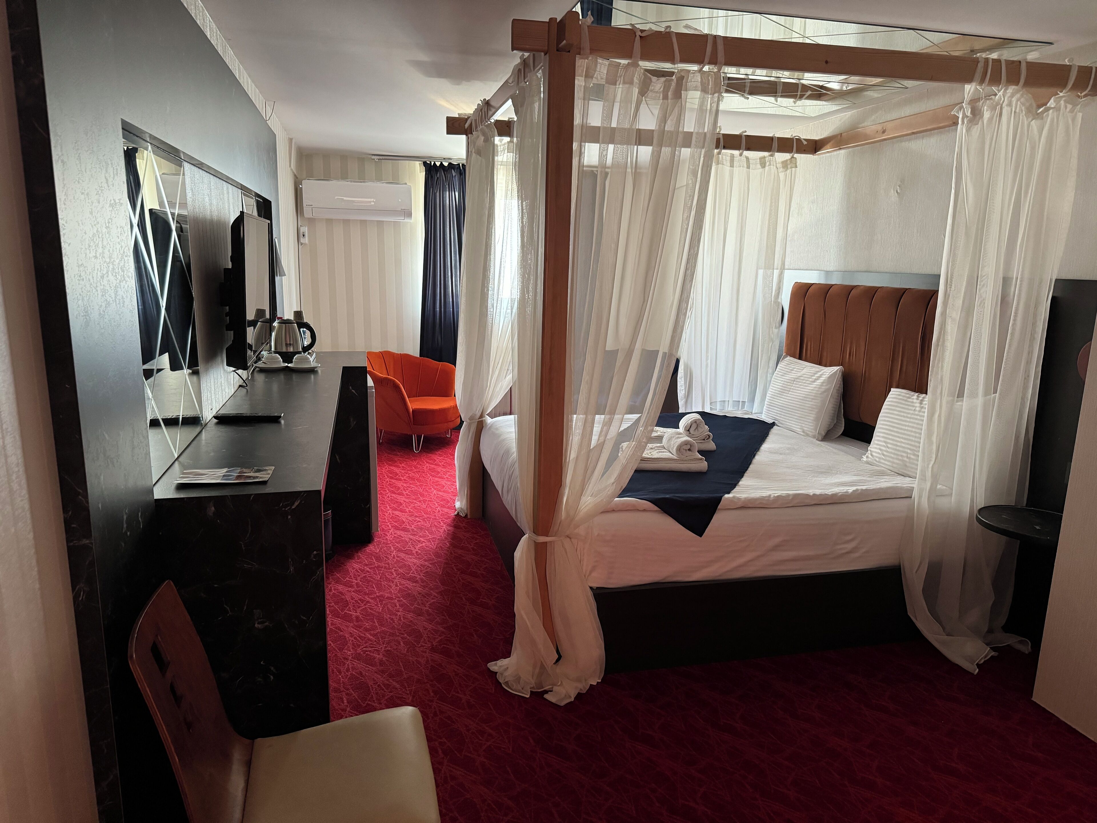 A hotel room with a four-poster bed, a desk with a chair, a coffee maker, and a television.