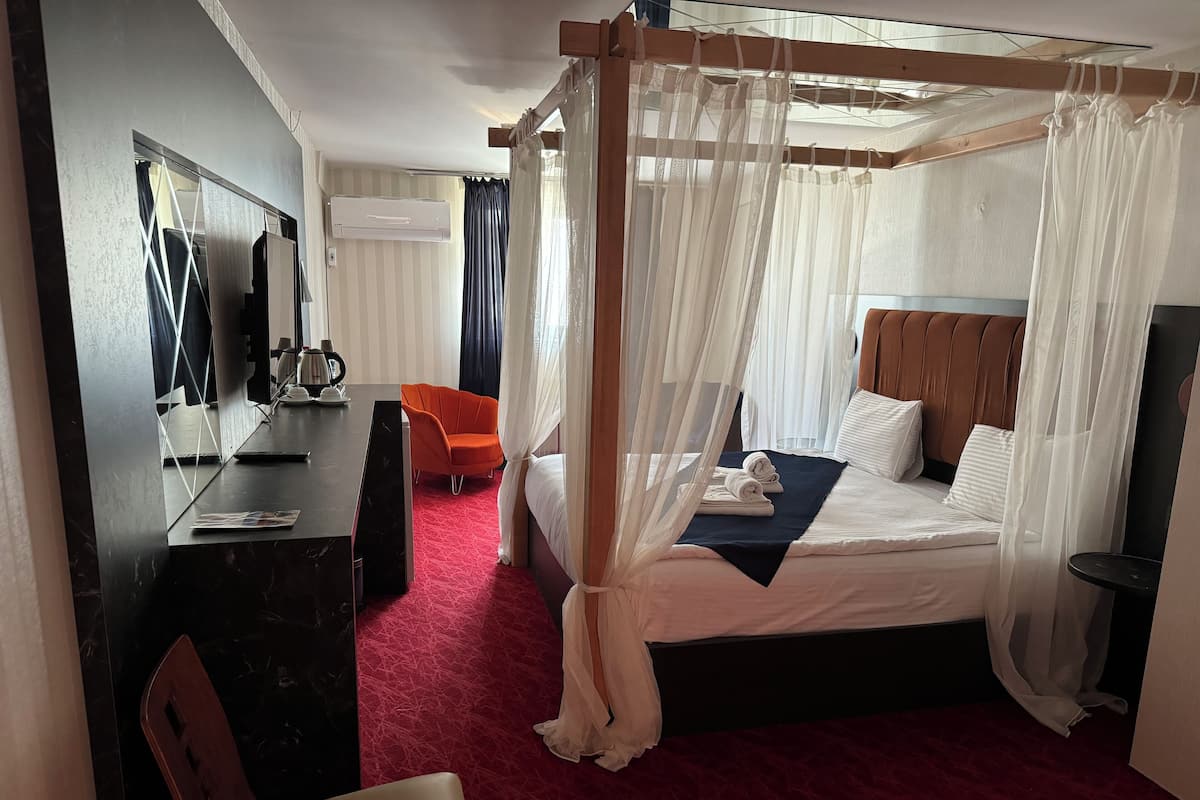 A hotel room with a four-poster bed, a desk with a chair, a coffee maker, and a television.