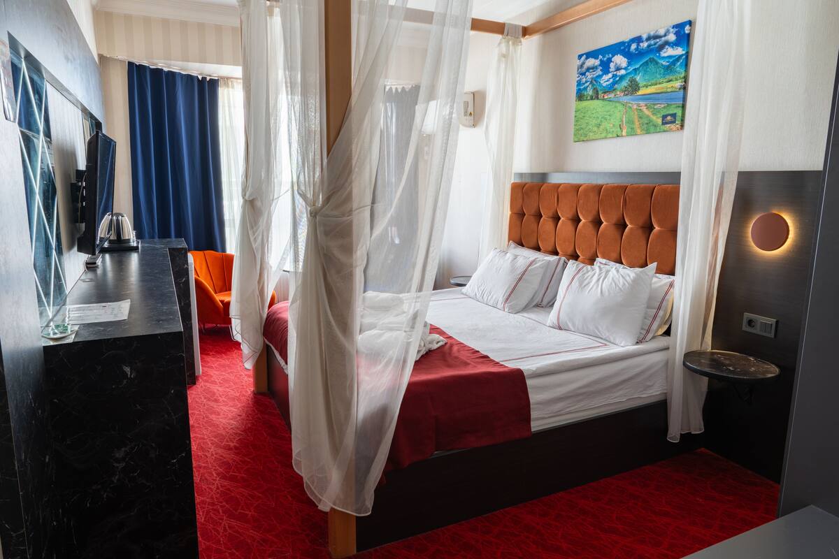 A hotel room with a bed, a desk, a chair, a TV, and a painting on the wall.