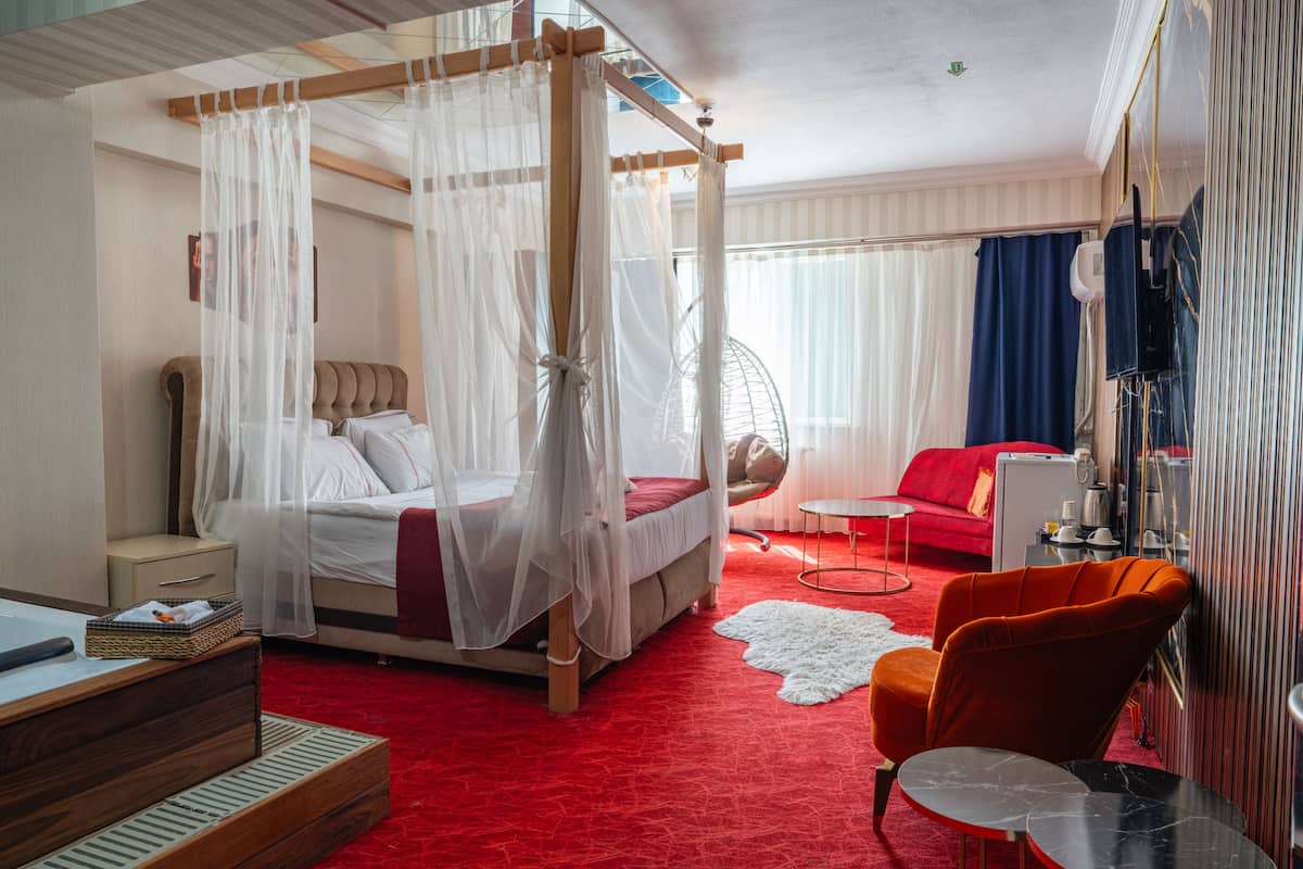 A bedroom with a four-poster bed, a red sofa, a small round table, and a chair.