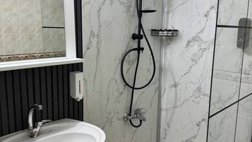 Une salle de bain moderne avec une douche en verre, un lavabo blanc et un mur recouvert de carreaux de marbre.