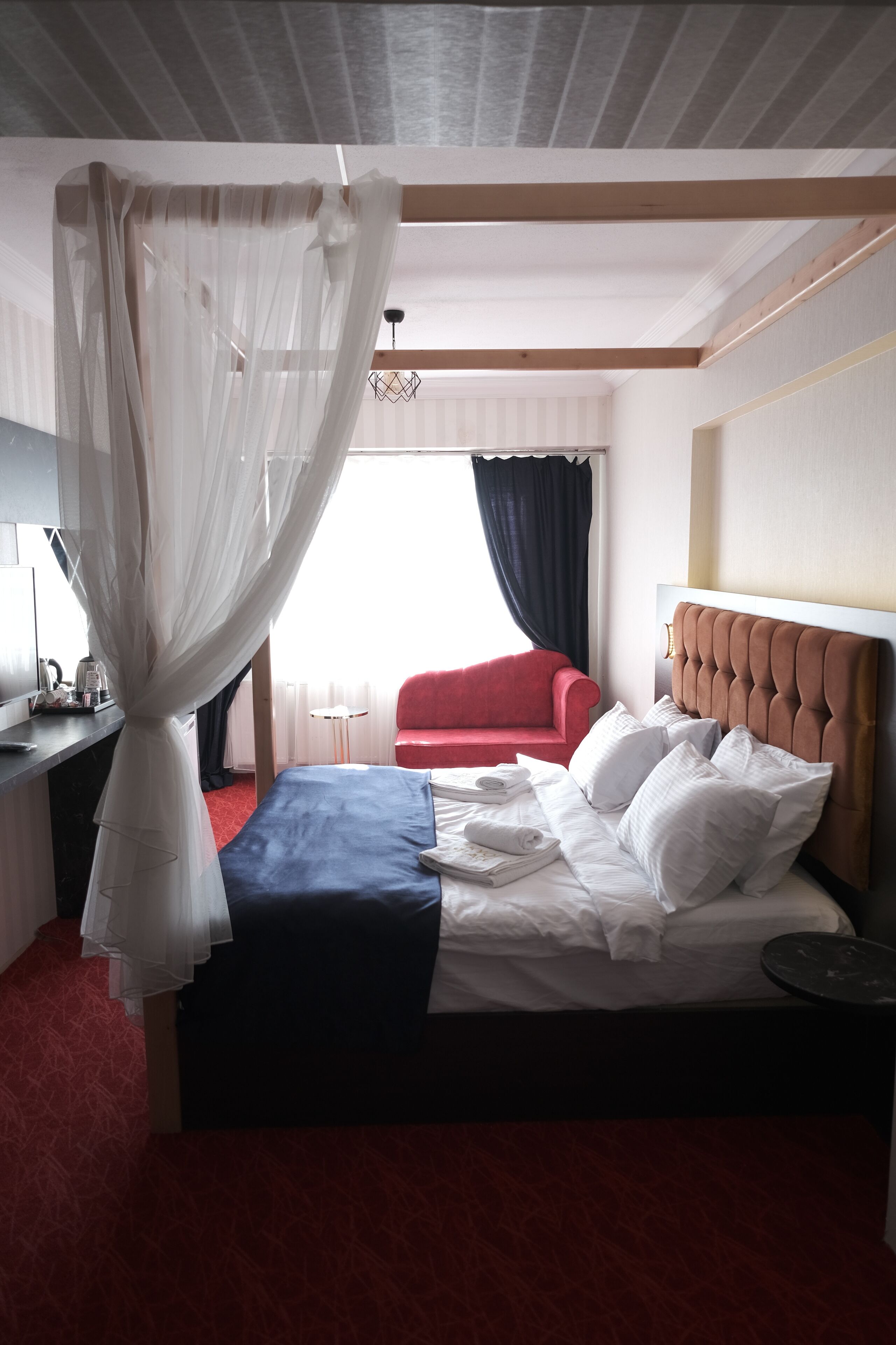 A hotel room with a bed, a red sofa, a TV, and a desk.