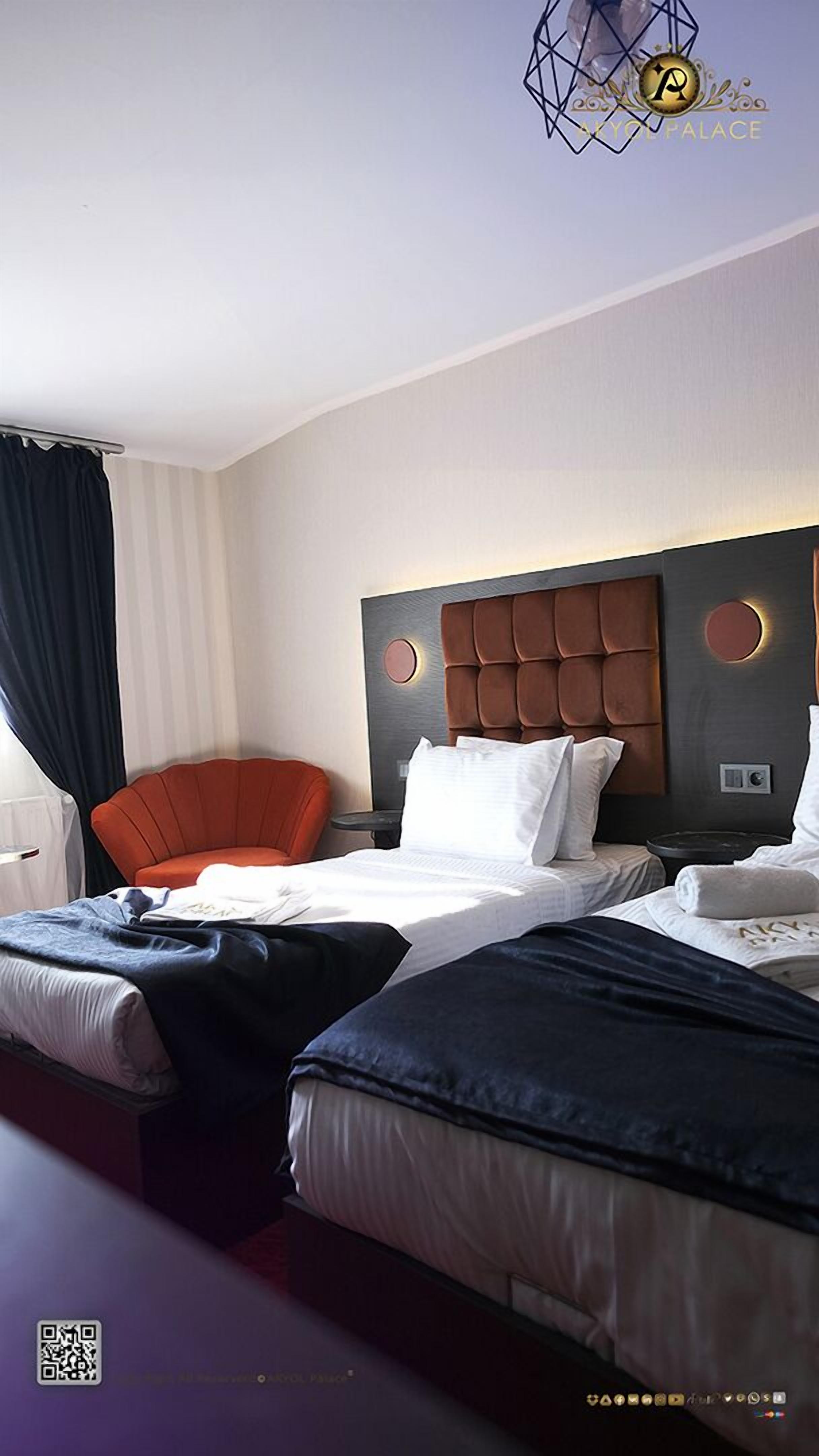 A hotel room with a large bed, a smaller bed, a red chair, and a round table.