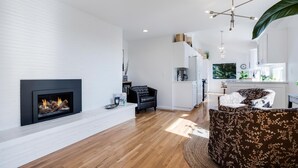 A modern living room with a fireplace, wooden flooring, and a large window. - Alder House: A Single Level Home in Dundee Hills (Dundee)