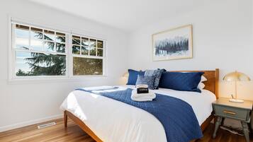 A bedroom with a large bed, a nightstand, a window with a view of trees, and a framed picture on the wall.