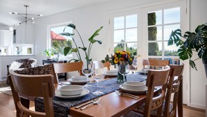A dining area with a wooden table set for four, surrounded by chairs. There are potted plants and a vase with flowers on the table. - Alder House: A Single Level Home in Dundee Hills (Dundee)
