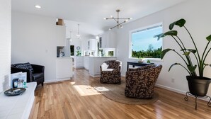A modern kitchen with white cabinets, a dining area with patterned chairs, and a large window with a view of greenery. - Alder House: A Single Level Home in Dundee Hills (Dundee)