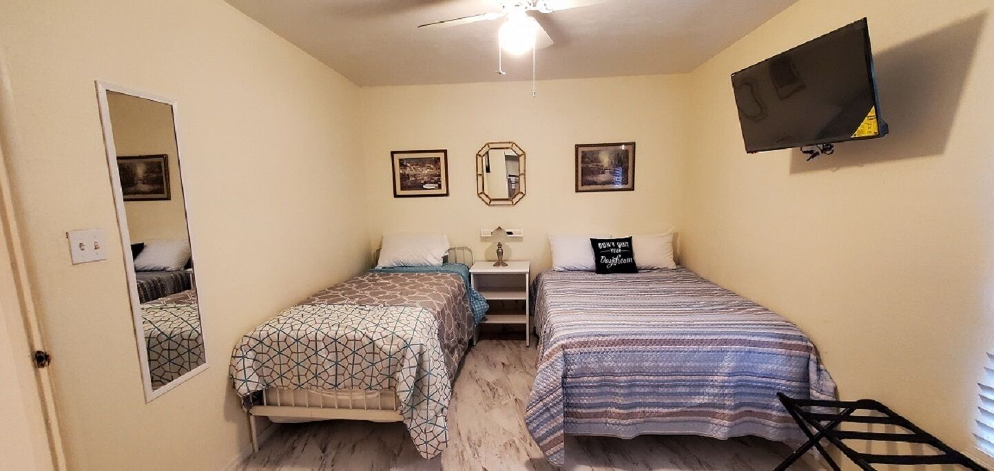 A bedroom with two beds, a TV, a mirror, and framed pictures on the wall.