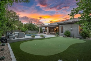 A backyard with a swimming pool, patio furniture, and a well-maintained lawn.