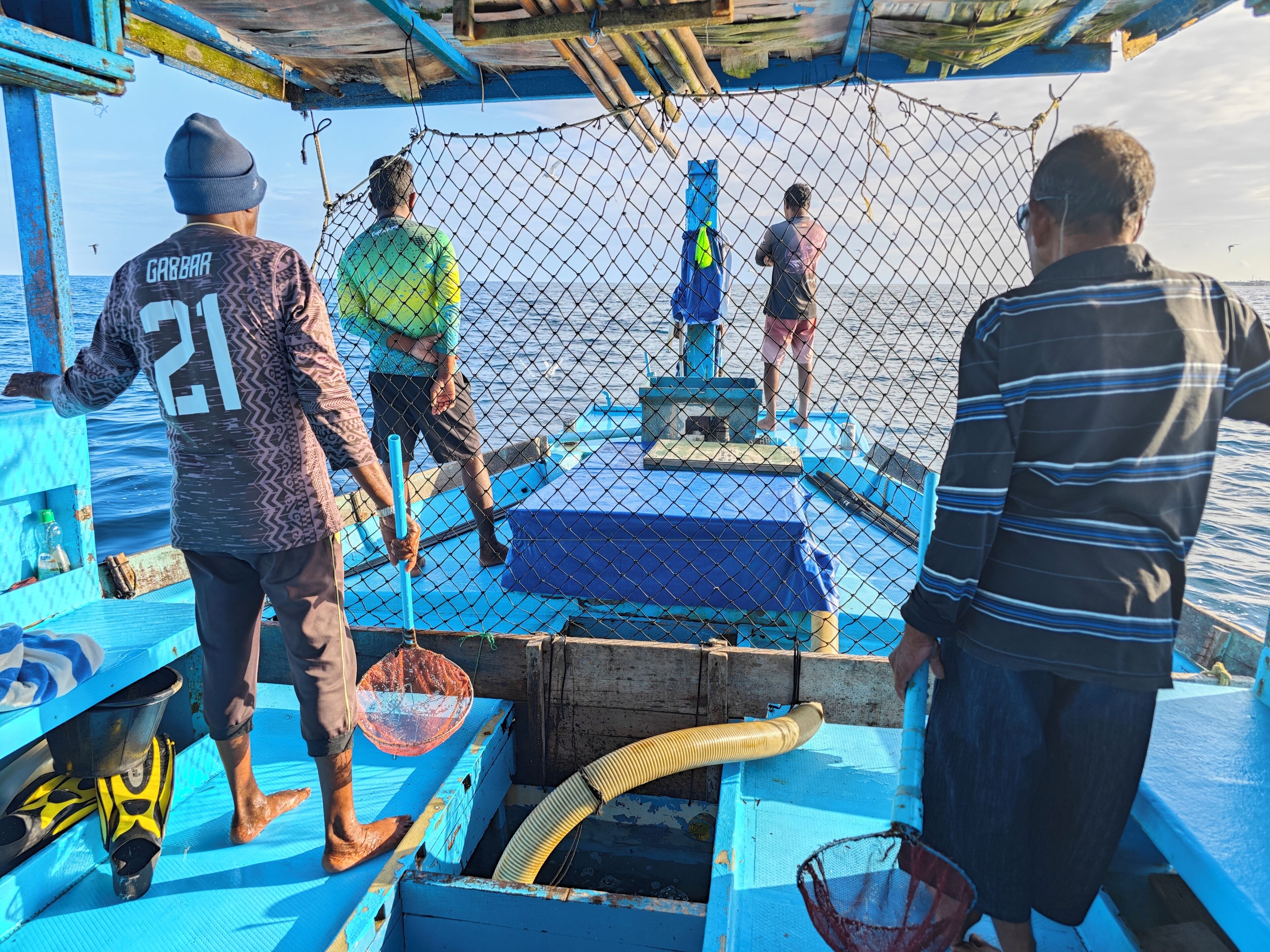 Un bateau de pêche avec un pont bleu, un filet et une personne portant un bonnet.
