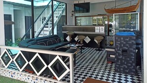 A modern hotel lobby with a checkered floor, a reception desk, a sofa, and a staircase leading to an upper level.
