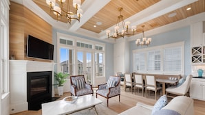 A spacious living room with a fireplace, comfortable seating, a dining area, and a kitchen with white cabinetry. - Beachtown - Stunning Beach Views - 3 Bedroom, 2.5 Bath (Galveston)