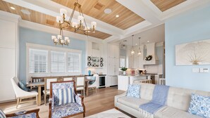 A spacious living room with a beige sofa, a wooden coffee table, and a dining area with a white table and chairs. - Beachtown - Stunning Beach Views - 3 Bedroom, 2.5 Bath (Galveston)