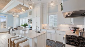 A modern kitchen with white cabinetry, a large island with stools, a gas stove, and pendant lighting. - Beachtown - Stunning Beach Views - 3 Bedroom, 2.5 Bath (Galveston)