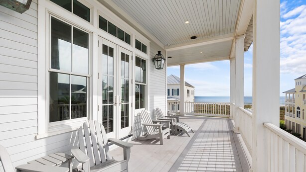 A covered porch with white wooden chairs and tables, large windows, and a view of the ocean. - Beachtown - Stunning Beach Views - 3 Bedroom, 2.5 Bath (Galveston)