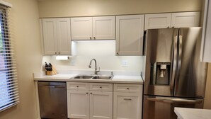 A modern kitchen with white cabinets, stainless steel appliances, and a wooden floor.