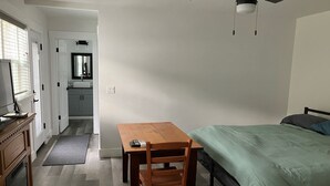 Een slaapkamer met een bed, een tafel en een stoel. Boven het bed hangt een plafondventilator.