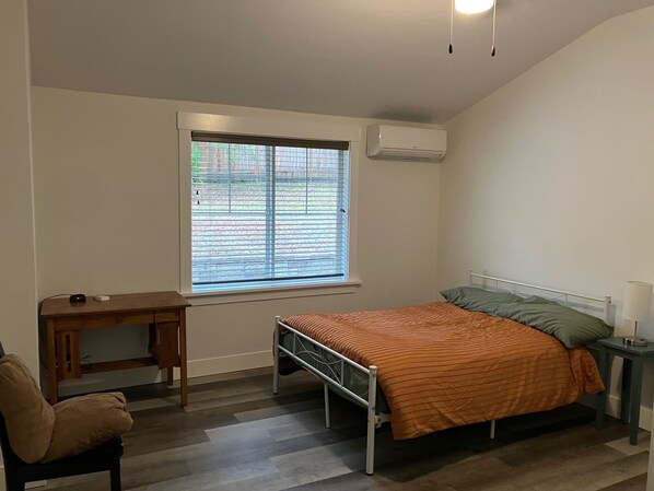 A bedroom with a bed, a desk, a chair, a window with blinds, and an air conditioning unit. - Beautiful Quiet Cozy  remodeled riverfront home. (Deadwood)