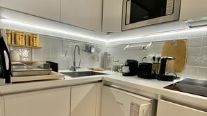 Uma cozinha moderna com armários brancos, micro-ondas embutido e iluminação LED sob os armários.
