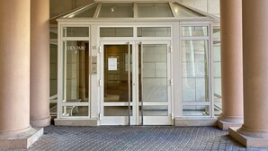 Entrada de um edifício com porta de vidro, colunas e piso de azulejos.