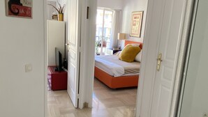 Um corredor que dá para um quarto com uma cama, uma escrivaninha e uma cadeira.