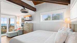 A bedroom with a large bed, a ceiling fan, a view of the ocean, and a window with blinds.