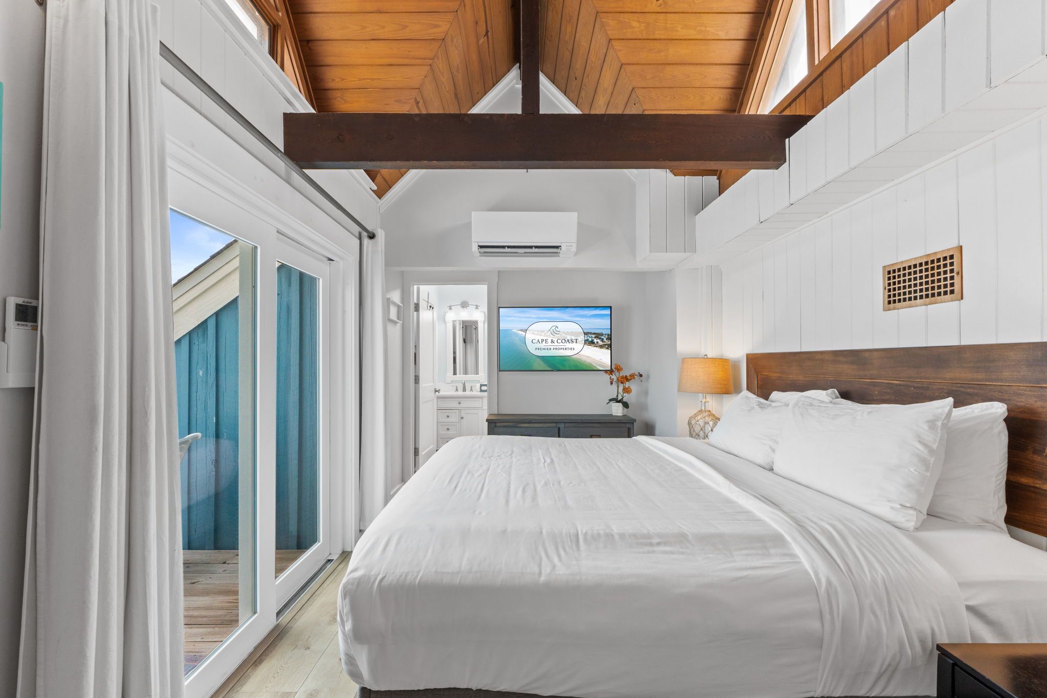 A bedroom with a large bed, a television, and a view of the sea.