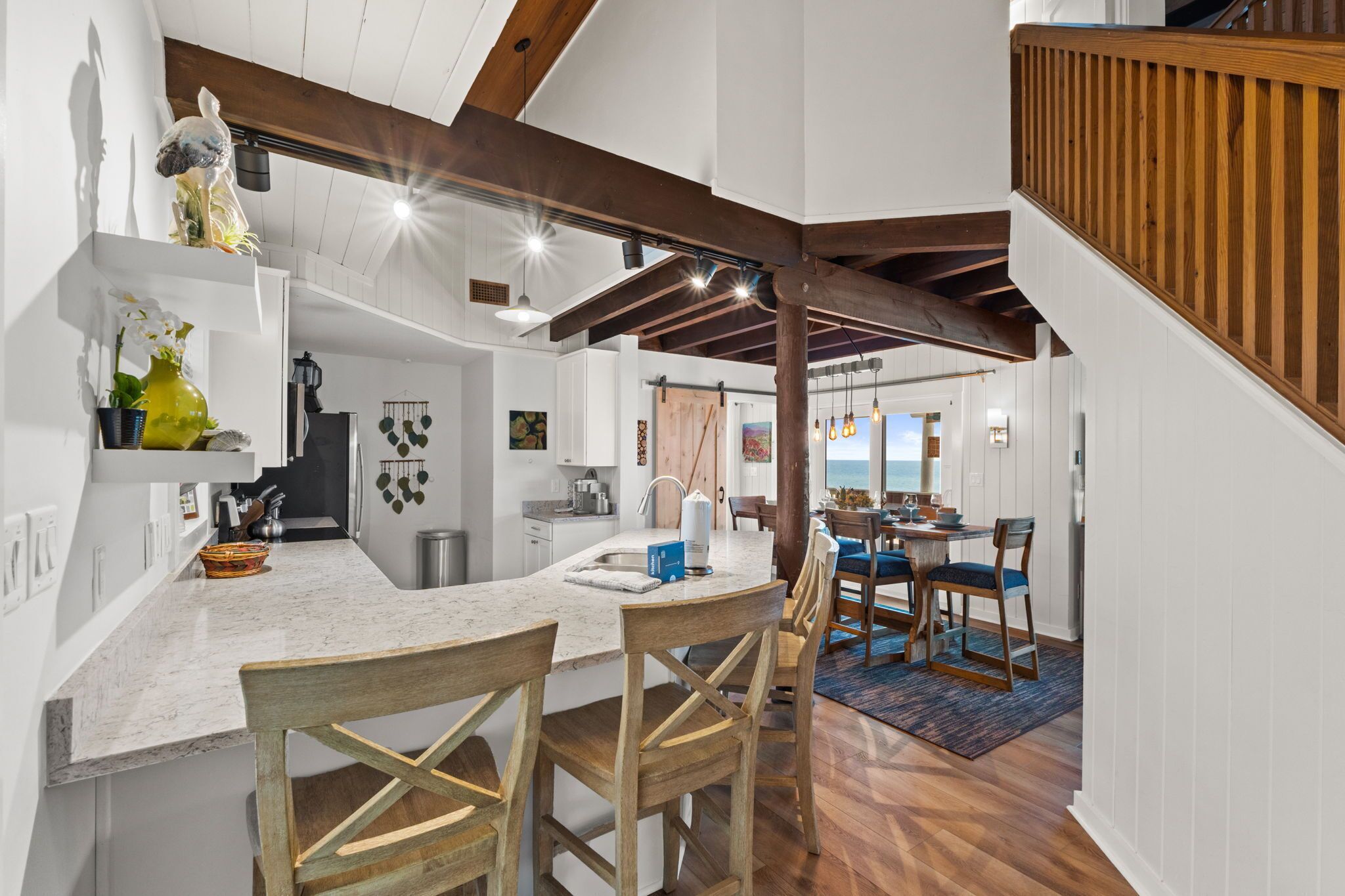 A kitchen with a marble countertop, wooden chairs, and a view to the dining area.