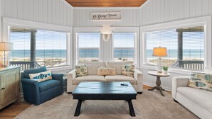 A spacious living room with a view of the ocean, a wooden ceiling, and a sign reading 'St. George Island'.