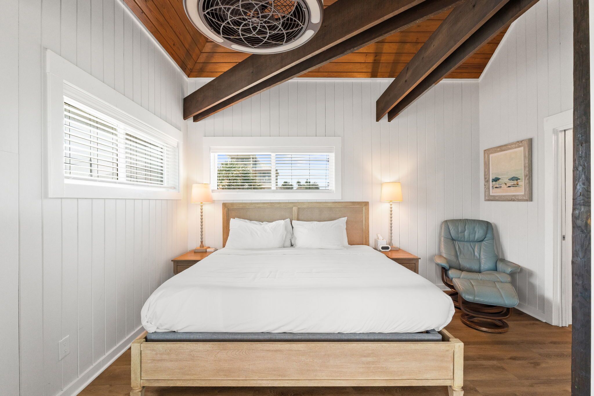 Quarto com estrutura de cama de madeira, duas mesas de cabeceira, uma cadeira e um ventilador de teto.