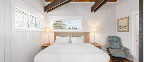 Quarto com estrutura de cama de madeira, duas mesas de cabeceira, uma cadeira e um ventilador de teto.